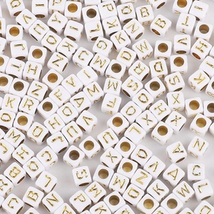 Macro shot of white acrylic cube beads with gold letters and central threading holes