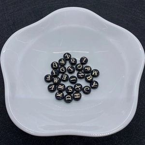 Detailed macro view of 8mm round black shell beads with gold letter engraving for jewelry