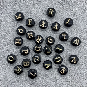 Macro shot of 8mm round black shell beads with golden A-Z letters for DIY necklaces