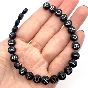 Detail of round black shell beads with gold-engraved A-Z letters for DIY jewelry