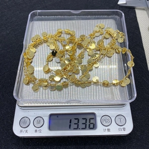 Detail shot of golden metal chain with small round pendants on an electronic scale