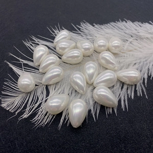 Macro view of teardrop faux pearl beads on white feather background for DIY jewelry