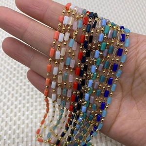 Hand holding colorful cylinder gemstone beads and golden copper chain roll for DIY jewelry