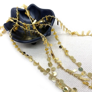 Golden twist round sequin chain jewelry accessory displayed on elegant ceramic plate