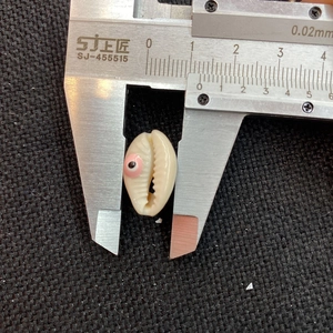 Macro view measuring a 10mm white seashell bead with pink evil eye detail using a caliper