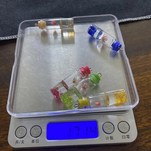 Five cylindrical glass resin pendants with colorful dried flowers shown on a scale