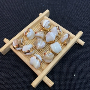 Detailed view of 12 irregular shell pendants with gold plated edges on a bamboo tray