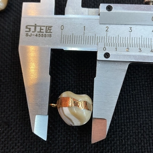 Macro shot of a heart-shaped striped shell pendant being measured with a caliper