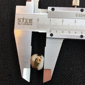 Macro shot of a 10mm white shell bead with gold metal rim being measured by a caliper