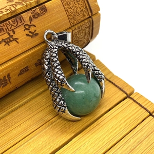Close-up of vintage silver dragon claw pendant holding a green stone on bamboo mat