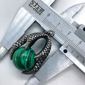 Macro detail of dragon claw pendant with green stone bead measured by a caliper