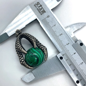 Macro detail of malachite stone dragon claw pendant being measured with a caliper