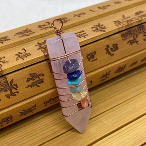 Macro detail of wire-wrapped rose quartz prism pendant with seven chakra stones on bamboo