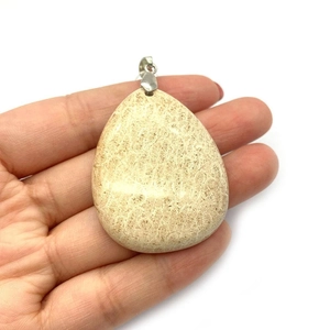 Vue détaillée d'un pendentif en pierre naturelle crème en forme de goutte tenu à la main
