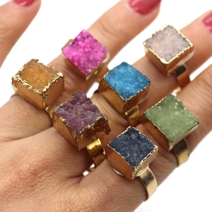 Dettaglio di sette anelli squadrati in pietra druzy colorata con bordi dorati lucidi