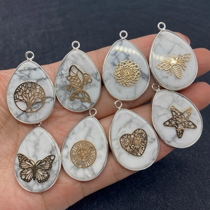 Natural white turquoise water drop pendants with gold patterns held in a hand