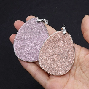 Pink and purple teardrop shell pendants with silver metal frames held in hand