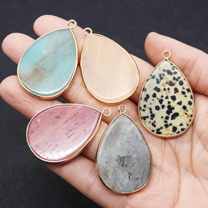 Macro detail of five teardrop gemstones with gold plating held in hand on dark background