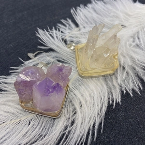 Natural amethyst and white crystal pendants with silver metal bases on a white feather