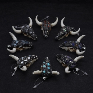 Vista de ocho colgantes de calavera de toro de resina con piedras de colores sobre negro