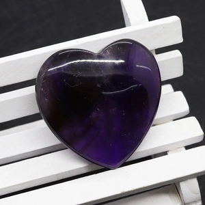 Pietra di ametista viola lucida a forma di cuore su una mini panchina bianca decorativa