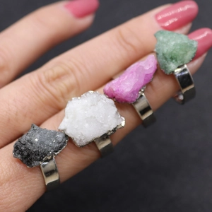 Hand wearing natural irregular crystal rings with raw stones in multiple colors and silver band