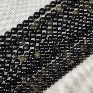 Close-up of golden sheen obsidian beads showing various sizes on grey linen fabric