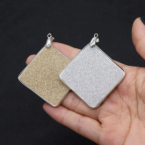 Hand holding square natural shell pendants in gold and silver with frosted matte finish