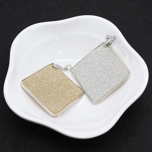 Gold and silver square shell pendants with glitter finish and metal frame on a white dish
