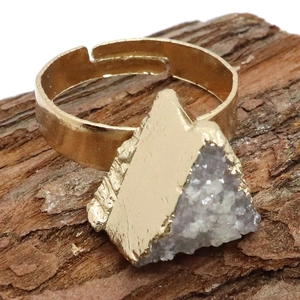 Primer plano de anillo ajustable dorado con piedra druzy triangular sobre fondo de corteza