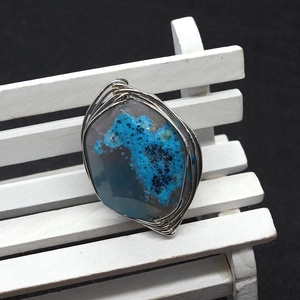 Macro detail of handmade wire-wrapped blue agate natural stone pendant on a wooden stand