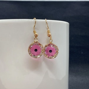 Macro shot of pink faceted crystal evil eye drop earrings on white ceramic edge