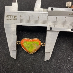 Macro shot of turquoise heart connector being measured with a digital caliper