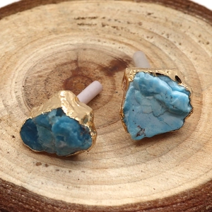 Irregular raw turquoise stud earrings with elegant gold trim on a natural wood background