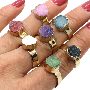 Close-up of seven assorted druzy crystal rings in gold finish on female fingers