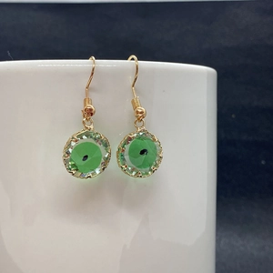Golden hook earrings featuring faceted green crystal Evil Eye charms on a ceramic display