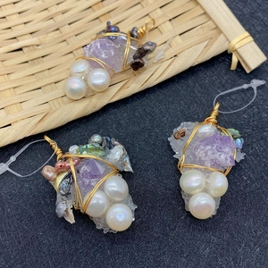 Handmade grape-shaped pendants with amethyst, pearls and gold wire on a textured background