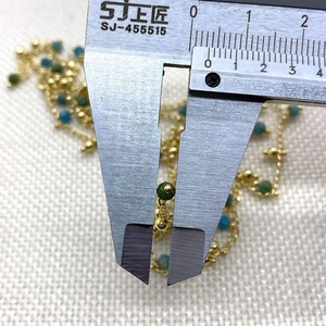 Detailed macro shot of 2mm green and blue beads on a delicate golden chain necklace