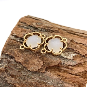 Macro detail of gold flower connectors with white stone inlays on a rustic wood stand