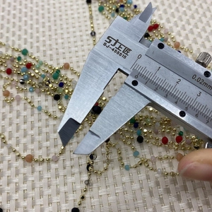 Detailed measurement of colorful stone beads on a golden chain with a caliper tool