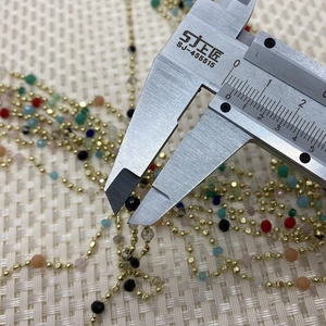 Macro detail of cursor caliper measuring 2.5mm natural stone beads on a gold metal chain