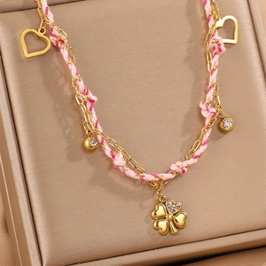 Collier tressé rose avec breloques cœur et trèfle sur support de présentation doré