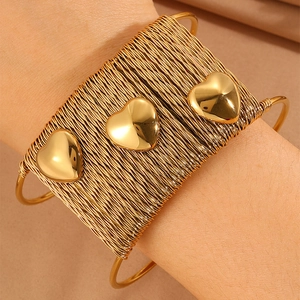 Detail of a gold braided open cuff bracelet featuring three polished heart charms
