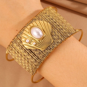 Close-up of golden woven metal cuff bracelet with scallop shell and pearl detailing