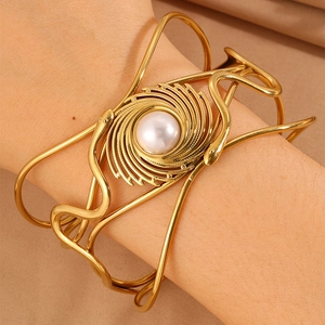 Macro shot of gold woven snake bracelet featuring a central pearl and intricate metal craft