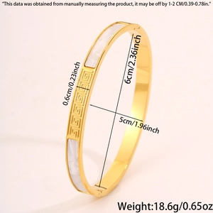 Detail view of gold stainless steel bangle with shell inlay and meander pattern engraving