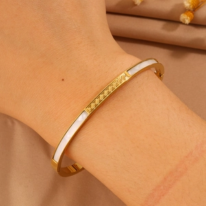 Detailed view of golden stainless steel bracelet with white shell inlay and Greek key motif