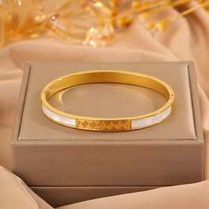 Detailed close-up of golden meander pattern bangle with white shell inlay on jewelry box