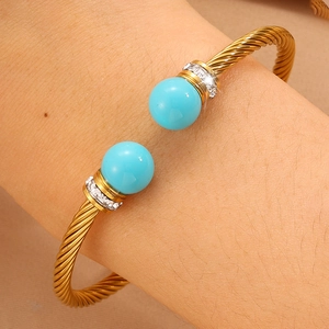 Détail d'un bracelet torsadé doré avec des pierres bleues et des accents de zircon