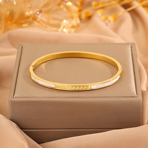 Close-up of golden stainless steel bracelet with white shell inlay and Greek key design